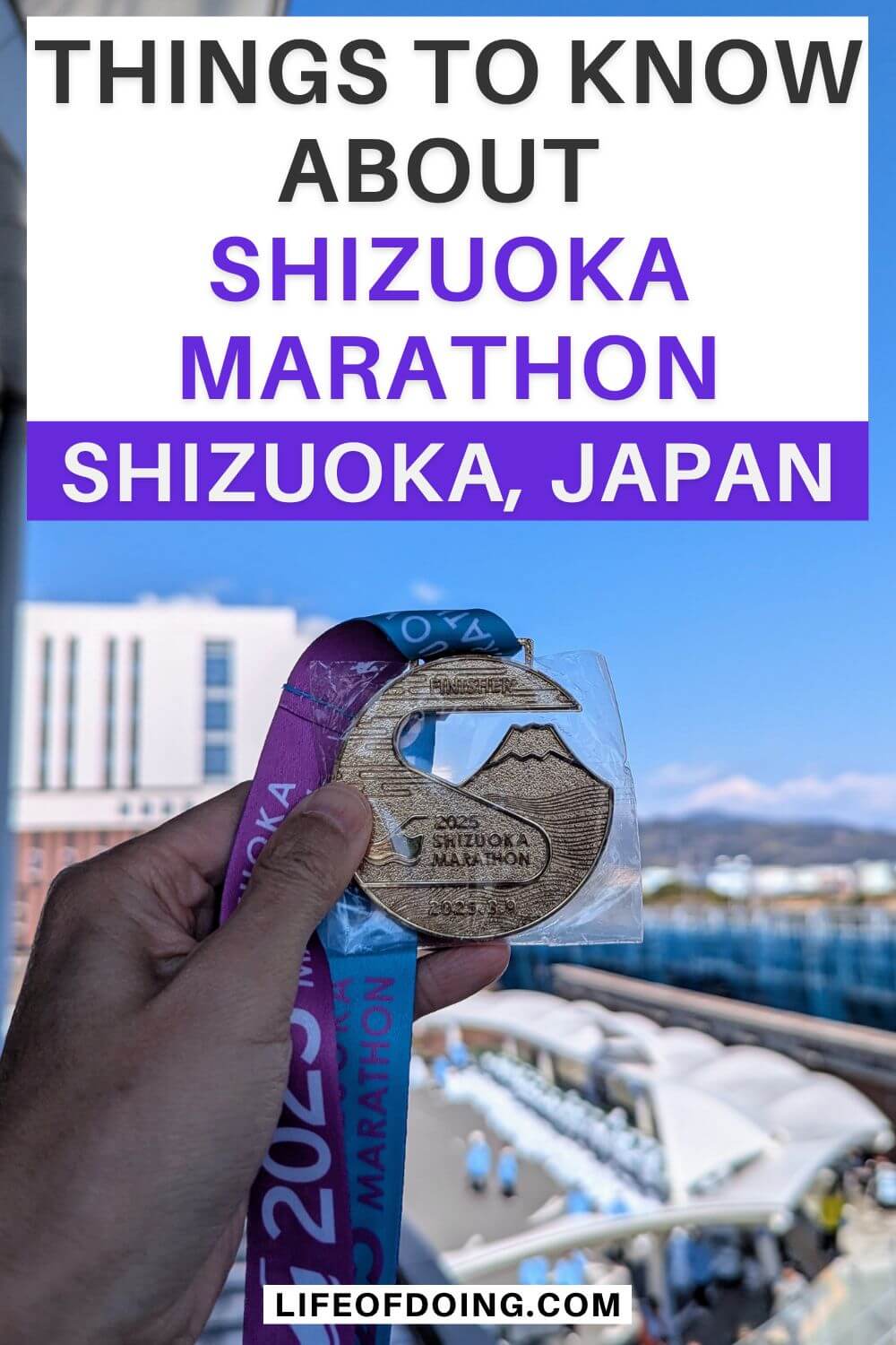 A hand holding the gold 2025 Shizuoka Marathon finisher medal with a purple and teal ribbon