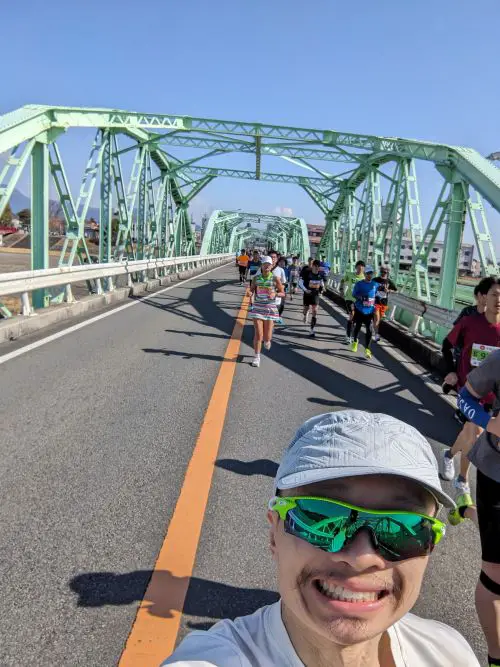 Justin Huynh, Life Of Doing, takes a selfie while running under a bridge on the Shizuoka Marathon 2025 course