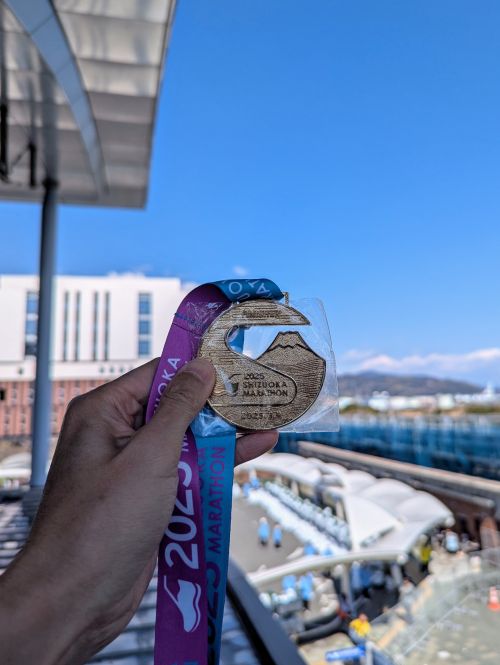 A hand holding the 2025 Shizuoka Marathon finisher medal
