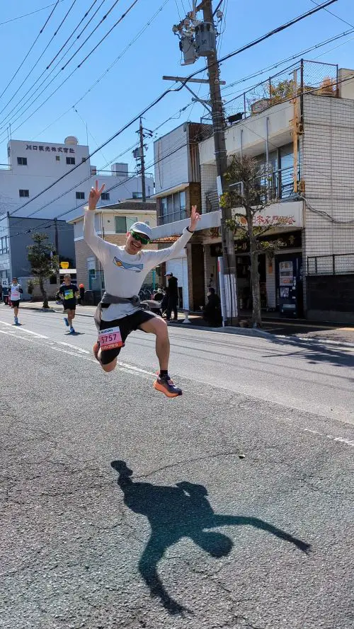 Justin Huynh, Life Of Doing, jumps and holds peace signs with his hands during the Shizuoka Marathon