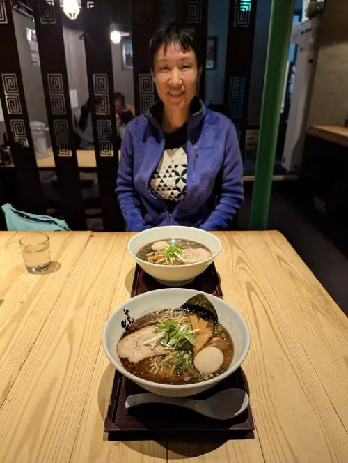 Jackie Szeto, Life Of Doing, smiles with two bowls of ramen with egg, bamboo, and charsiu at Ramen Yabuki Shizuoka