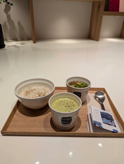 A wooden tray with three bowls: sesame rice, edamame and green pea potage soup, and fish soup from Soup Stock Tokyo Shizuoka