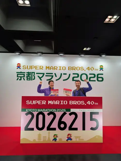 Jackie Szeto and Justin Huynh, Life Of Doing, stand at the Super Mario Bros. 40th Anniversary sign at the Kyoto Marathon Expo