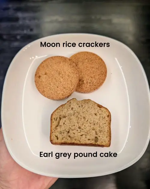 A hand holding a plate with two type of snacks - moon rice crackers and earl grey pound cake