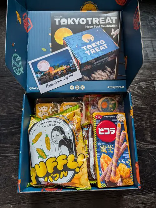 An opened TokyoTreat subscription box with the pamphlet, postcard, and snacks